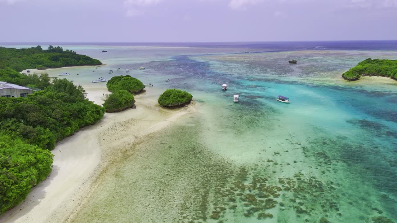 An aerial view of Kabira Bay in Ishigaki, Japan, with turquoise water and lush green islands. Glass-bottom boats float peacefully in the scenic bay