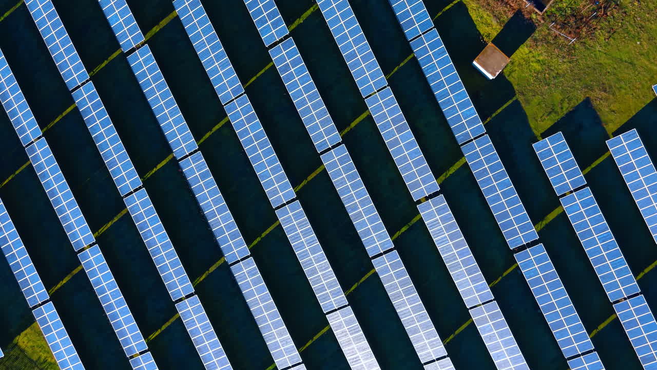 Fila diagonali di pannelli fotovoltaici da prospettiva aerea. Primo piano dall'alto di schiere di pannelli solari installati su erba verde che creano motivi diagonali geometrici.