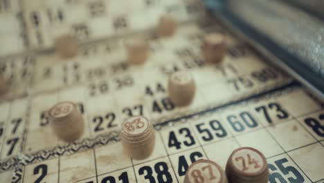 Macro-video-of-a-Bingo-board,-studio-lights,-120-fps,-slow-motion,-wooden-chip-digits,-Raw-footage,-lottery-desk-game,-card-numbers,-crane-pull-back-smooth-rotate-movement