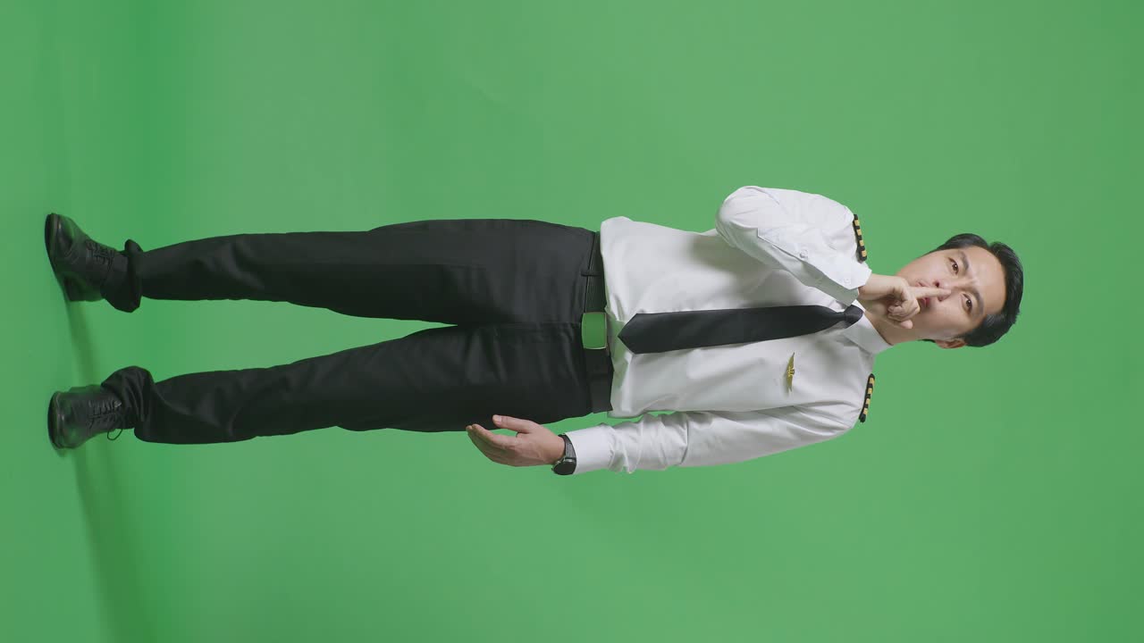 아시아 남성 조종사가 카메라를 바라보고 녹색 스크린 배경 스튜디오에서 shh 제스처를합니다.