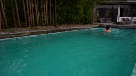 woman swims in relaxing swimming pool in luxury hotel surrounded by bamboos