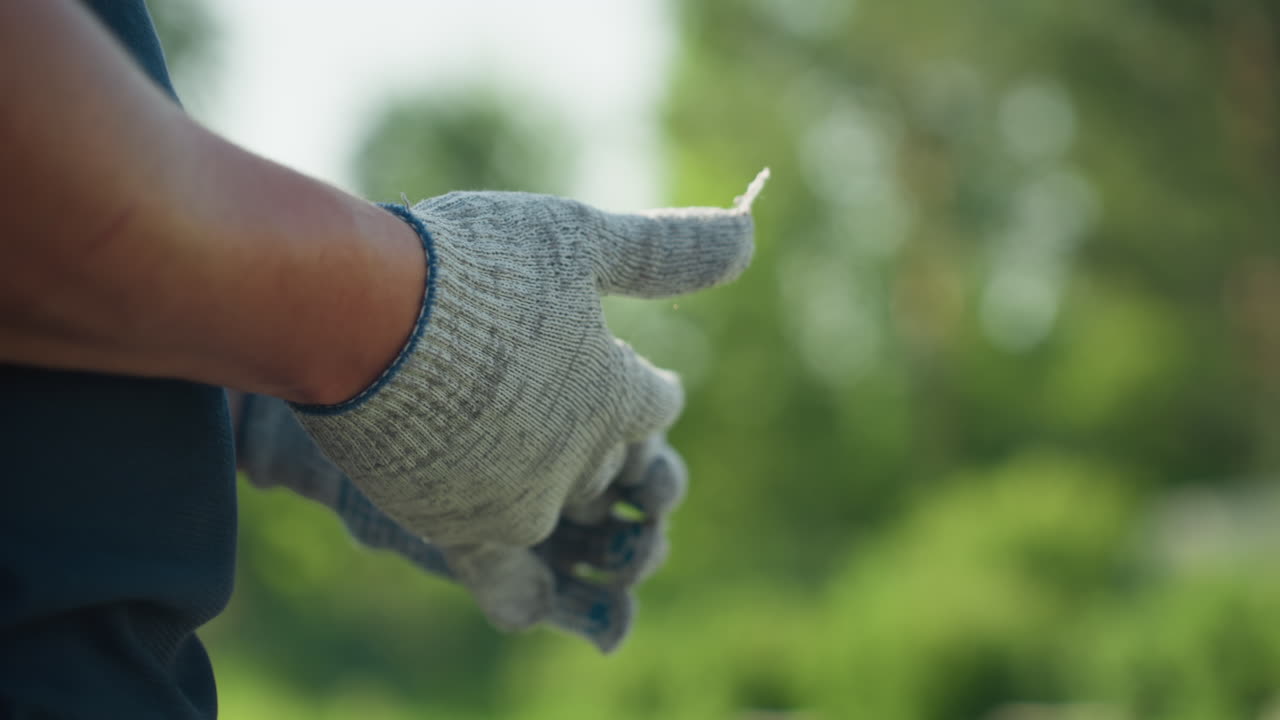 close up of fair skinned man removing glove from hand after outdoor work, soft background blur of greenery, focus on fingers and skin texture, moment of pause showing end of task