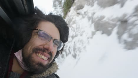bearded male wearing glasses smiling with head out of open window on train