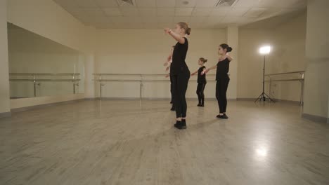 a group of young ballet students in black dancewear practicing positions in a spacious ballet studio with wooden flooring and wall-mounted barres. focused expressions and synchronized movements.