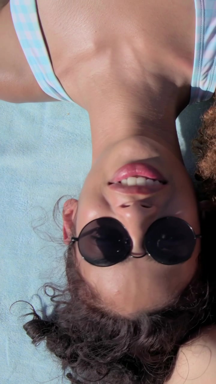 Vertical video: Camera widening revealing women sunbathing on beach mat with sunglasses and bikinis