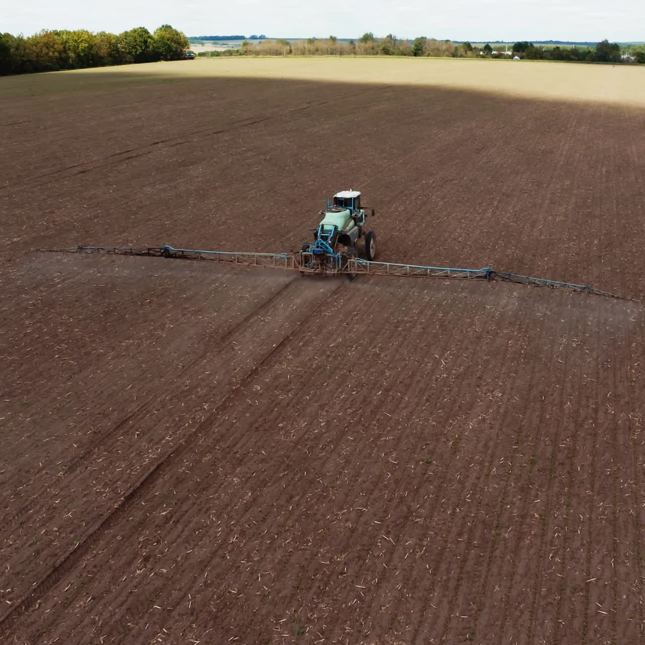Agricultural field in spring. Tractor with special equipment spraying field. Flying over the field with machinery sprinkling chemicals during seasonal works. Aerial view.