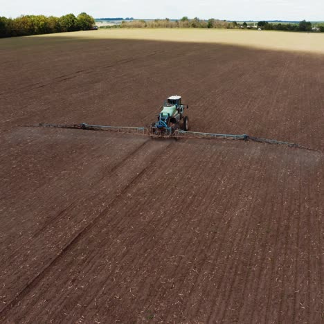 agricultural field in spring. tractor with special equipment spraying field. flying over the field with machinery sprinkling chemicals during seasonal works. aerial view.