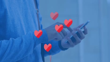 Animation-of-hearts-floating-over-hands-of-caucasian-man-using-smartphone