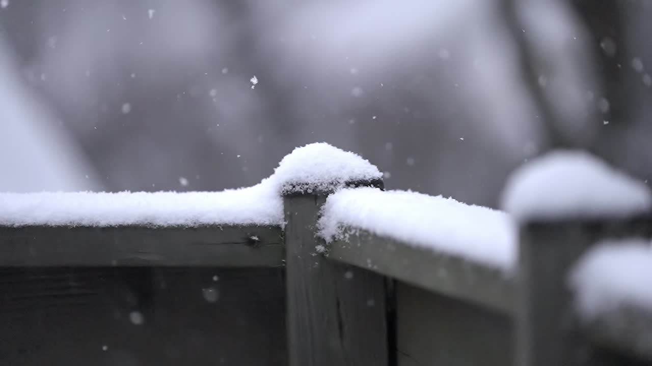 Snowfall on a railing, cold winter day, slow motion shot of small snowflakes falling outside on a wooden railing, static shot, copy space