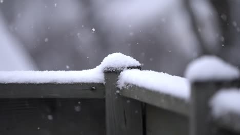 snowfall on a railing, cold winter day, slow motion shot of small snowflakes falling outside on a wooden railing, static shot, copy space
