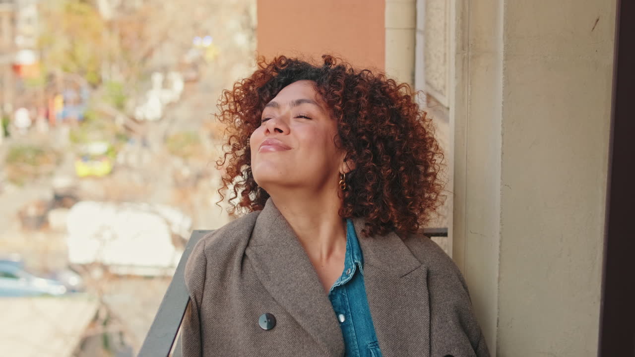 Serene Young Woman with Curly Hair Enjoying the Sun on a Balcony