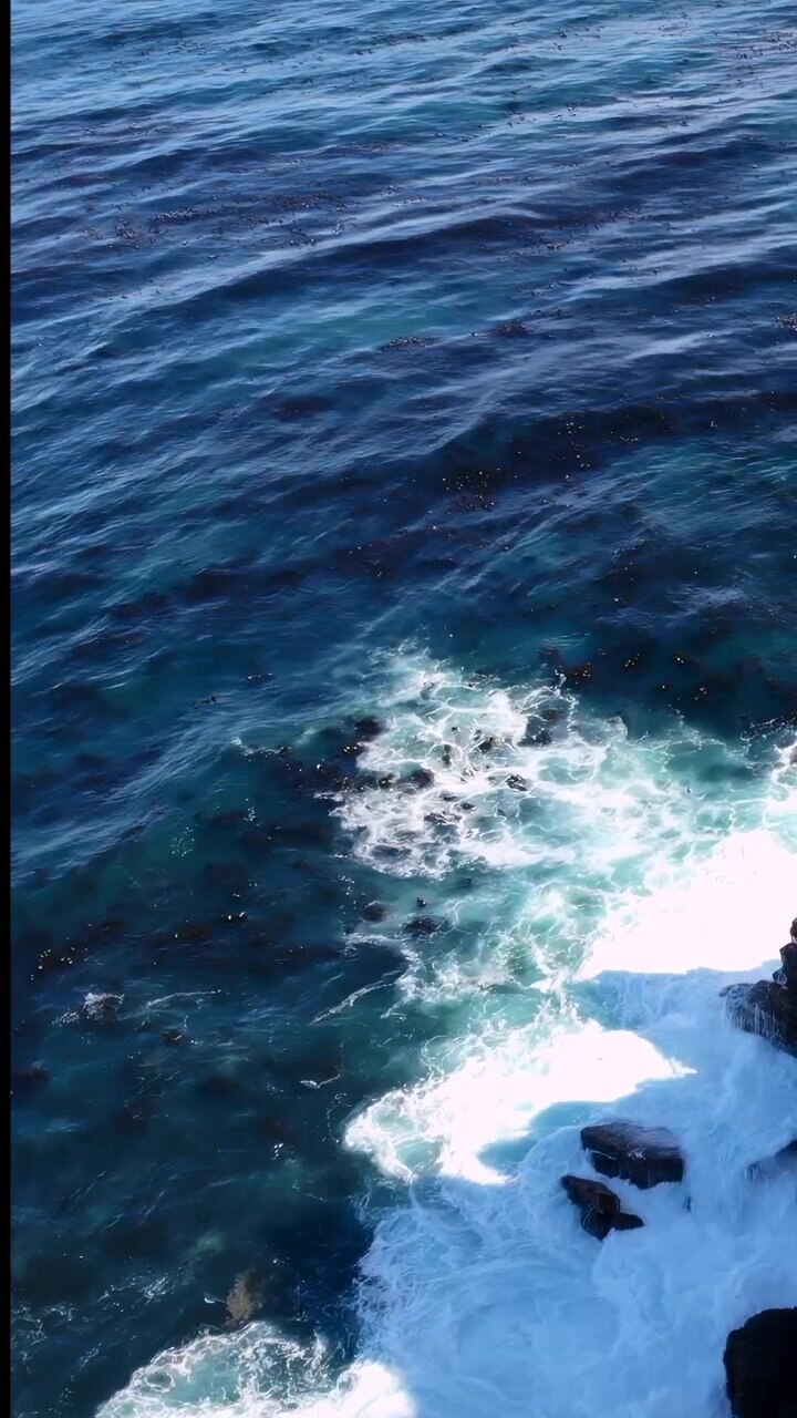 Costa rocciosa aerea con onde che si infrangono, spruzzi d'oceano turchesi che colpiscono scogliere di granito frastagliate, Drone