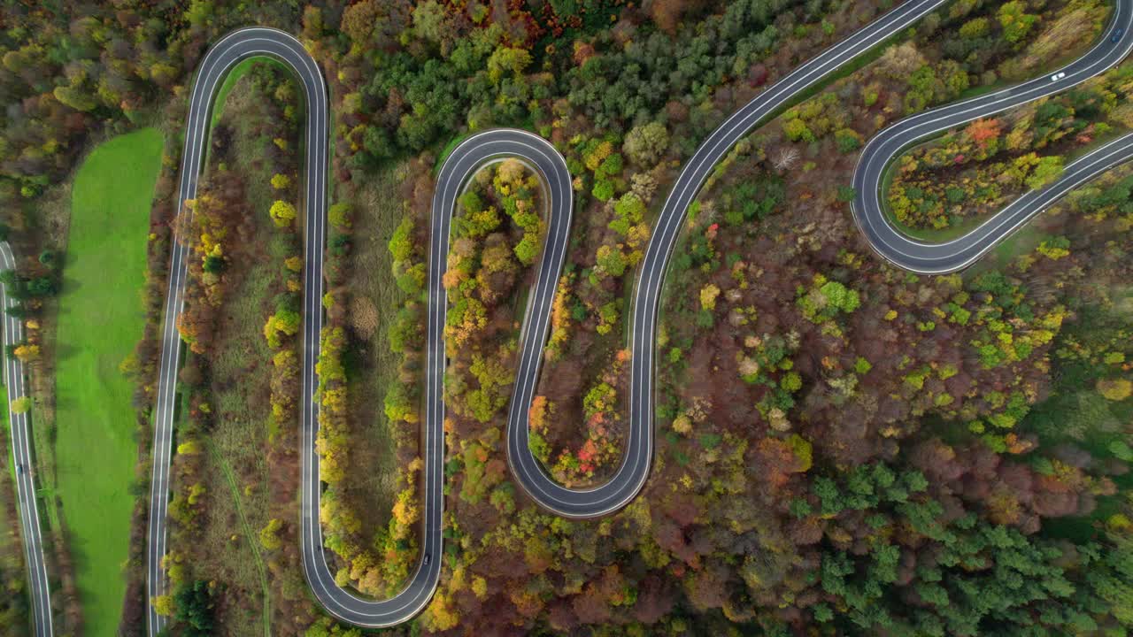 antena de arriba a abajo sobre un sinuoso camino de montaña rodeado por un bosque con árboles de otoño en las montañas de bieszczady en polonia, europa
