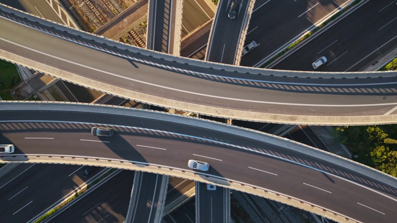Striking aerial top-down view of a complex multi-level highway interchange with cars and trucks driving along the curved overpasses and roads during a sunny day with long shadows
