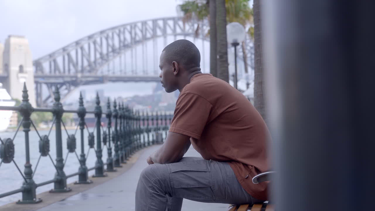 Opname van een Afrikaanse man zittend in Sydney, Australië, nabij de Harbour Bridge
