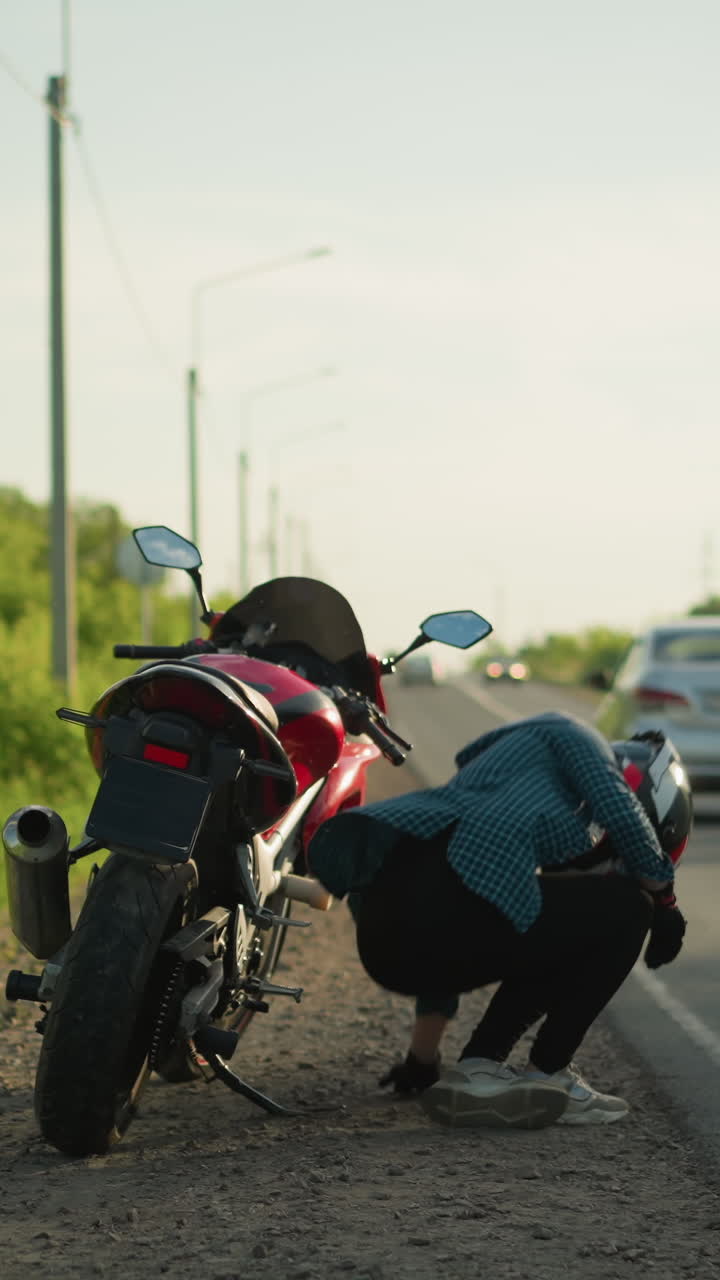 una dama con casco y camisa a cuadros camina por una carretera rural hacia su bicicleta eléctrica roja estacionada, descansa la espalda en la bicicleta, mientras un coche pasa en el fondo
