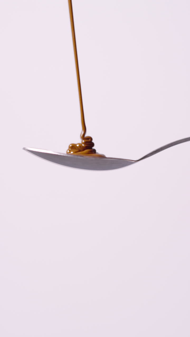 Vertical Video Of Melted Chocolate Being Poured Onto Spoon And Overflowing Against White Background With Copy Space