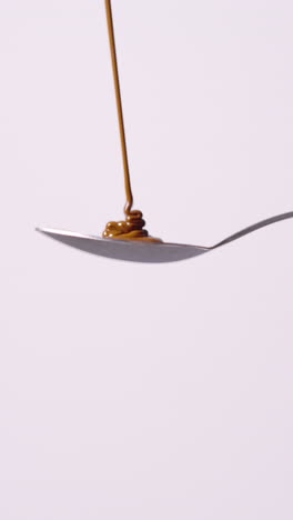 vertical video of melted chocolate being poured onto spoon and overflowing against white background with copy space