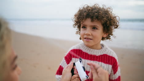 retrato adorable niño rizado descansando en la playa con la madre. niño enfocado sosteniendo cometa