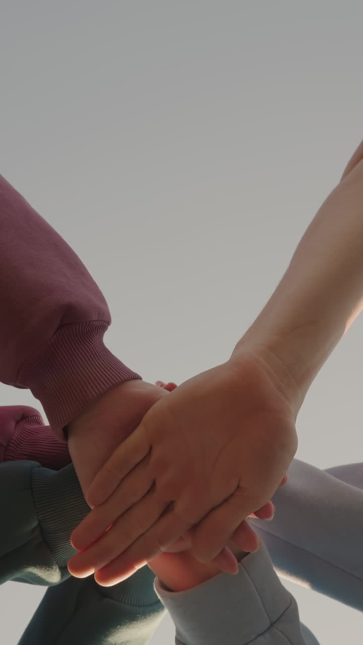 vista hacia arriba de personas con capuchones colocando sus manos juntas como miembros del equipo con la luz del sol creando un efecto de brillo alrededor de sus manos, simbolizando la unidad, el trabajo en equipo y la colaboración
