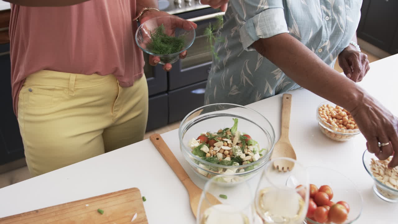 Midsection of senior african american female friends preparing salad in kitchen, slow motion