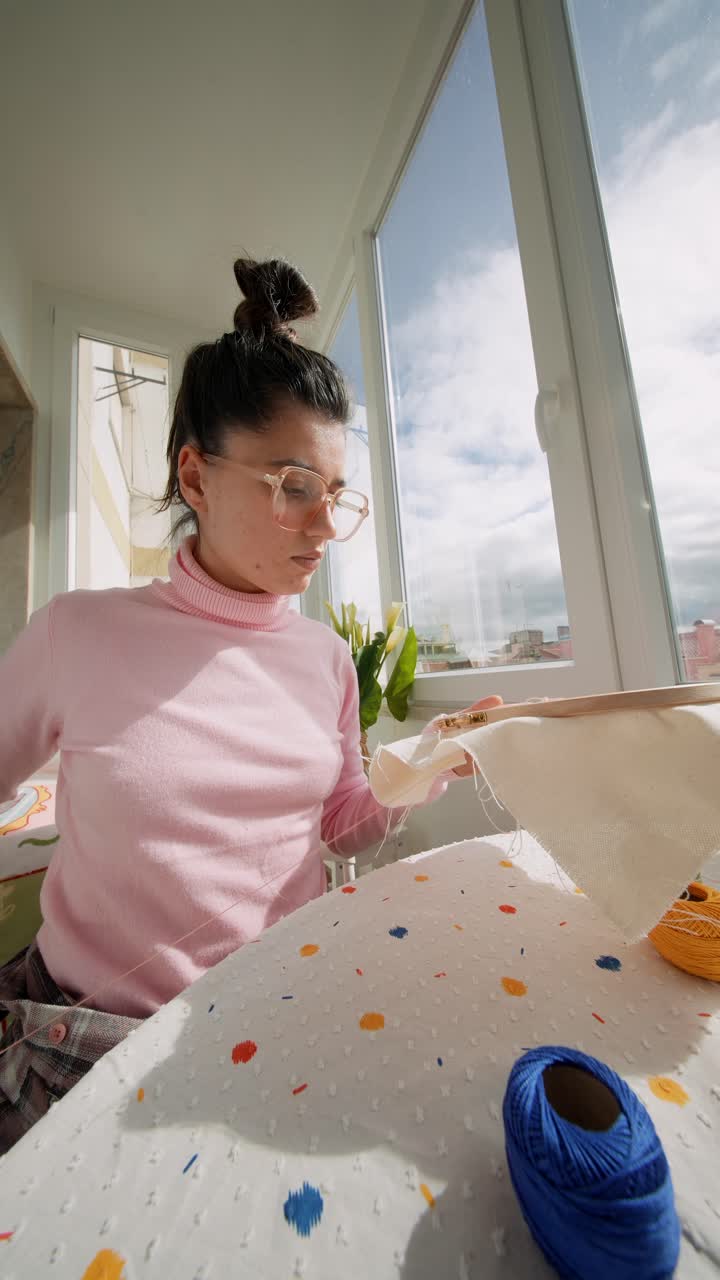 Young Woman Embroidering Fabric with Needle and Thread by Window