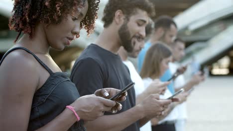 Serious-young-woman-using-smartphone-and-talking-with-friend