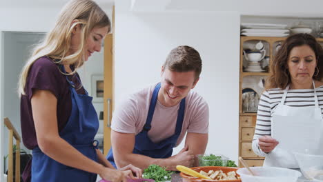 male and female adult students preparing ingredients for dish in kitchen cookery class