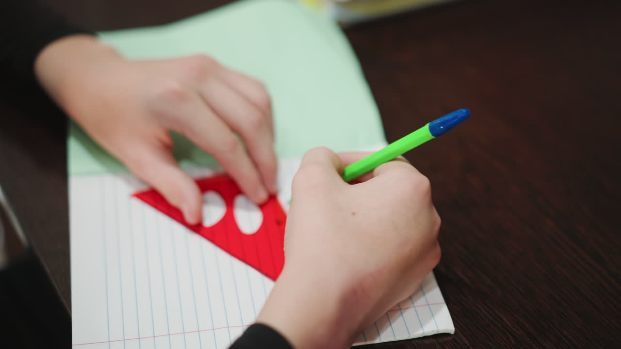 Grandma guiding grandson drawing paper heart, closeup hands on dark table with lined notebook and green paper, red heart cutout traced with bluetipped pen, tender teaching moment of homemade keepsake