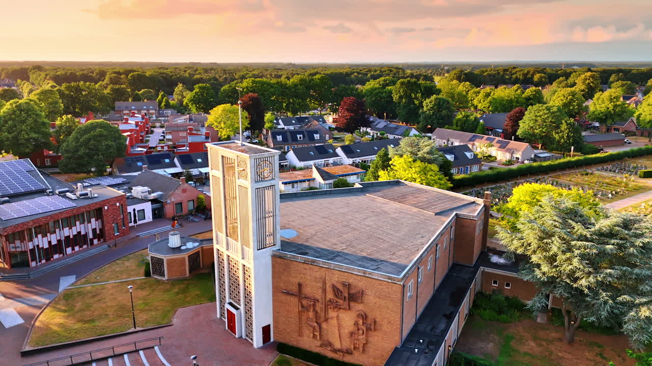 Flying around the unusual building of the church in Overloon, Netherlands. Sun-dazzled scenery of the village at sunset time