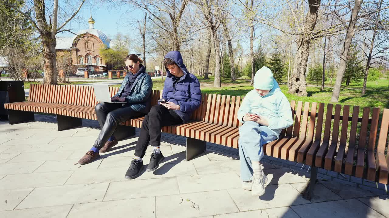Tre personer bruger digitale enheder på en parkbænk