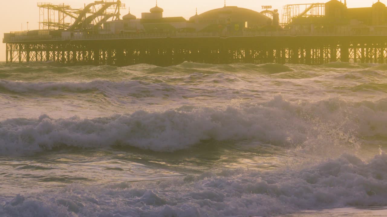 Big Slow Motion Sea Waves Crashing on Brighton Beach with Palace Pier in Background at Sunset. Natural Ocean with Historic Seaside Building in United Kingdom