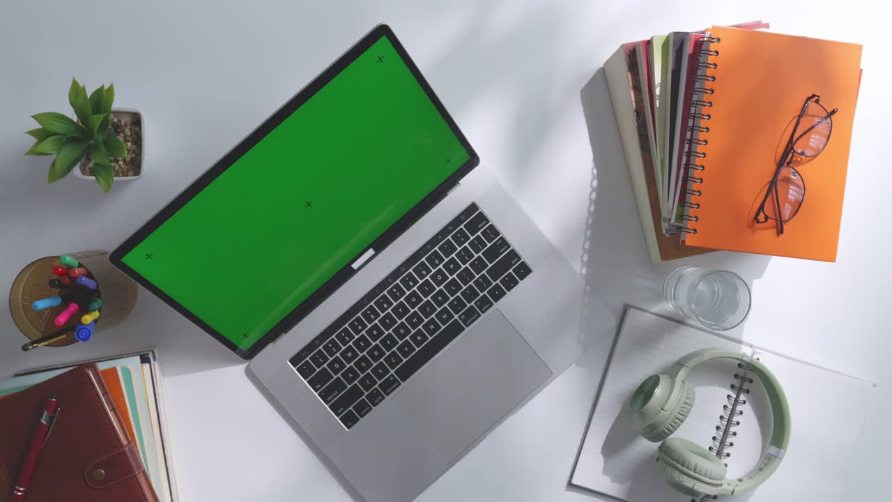 portátil con pantalla verde en un escritorio con libros y accesorios