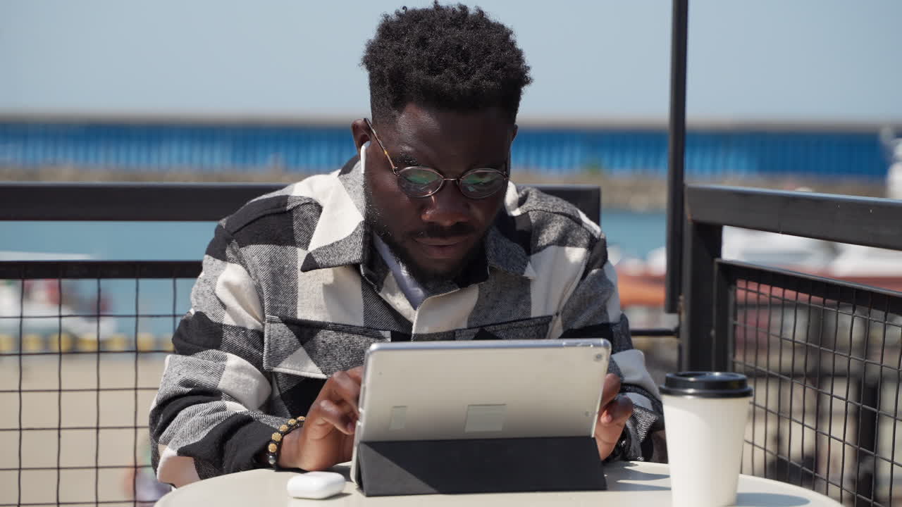 Man working outdoors on a tablet in a cafe.