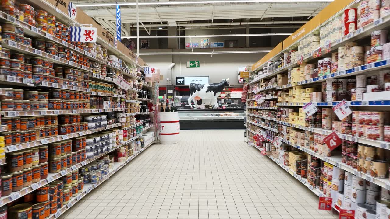 A steady camera moves forward through a brightly lit grocery store aisle with stocked shelves
