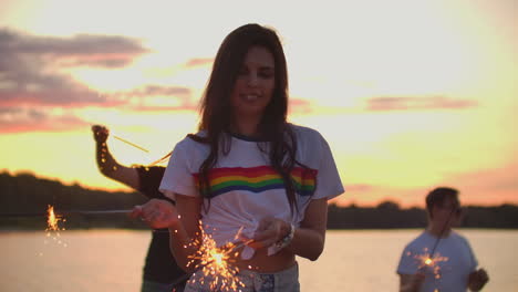 los adolescentes están bailando con grandes luces bengalíes en la costa de arena. esta es una loca noche de verano en la fiesta al aire libre.