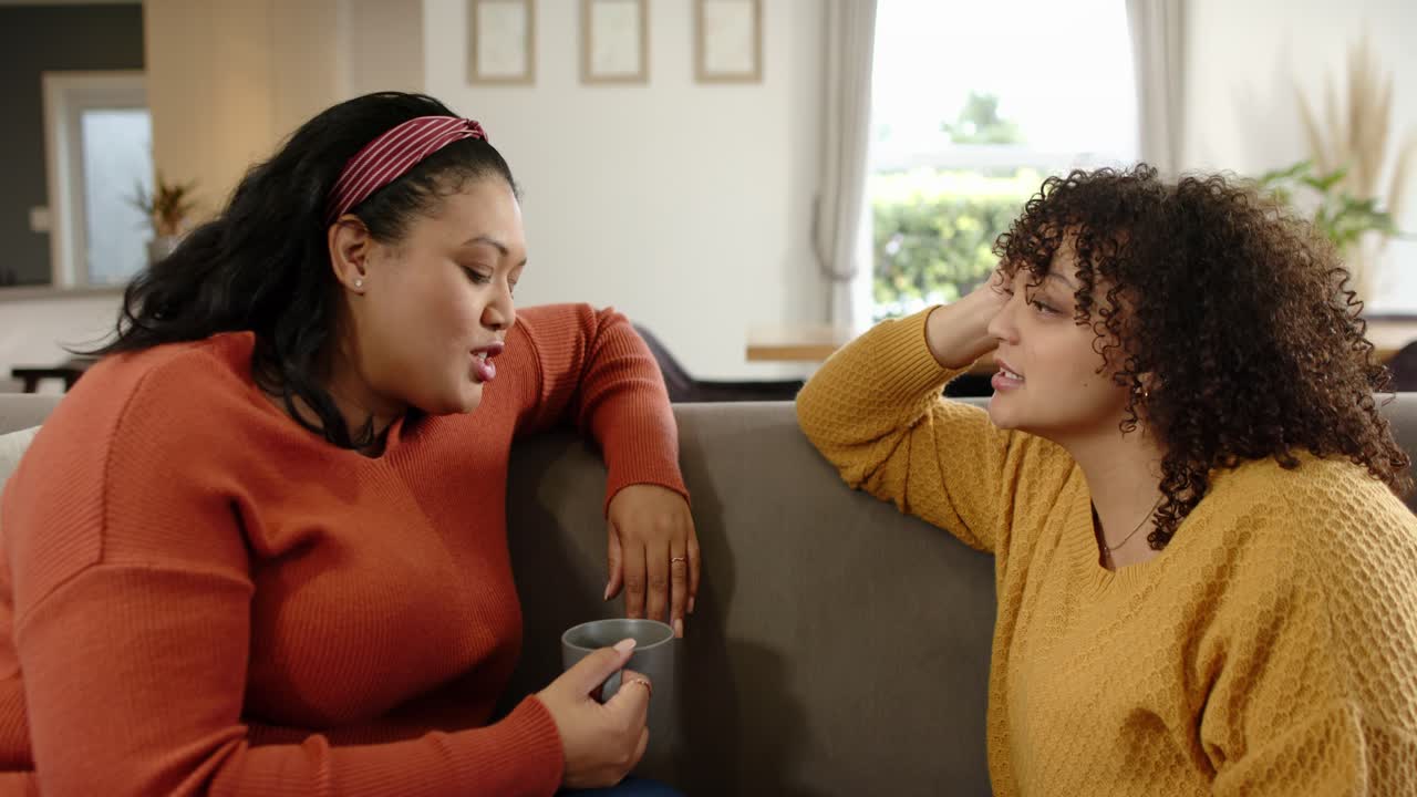 Mother and daughter laughing after remark while mother narrating story sipping ceramic mug on couch