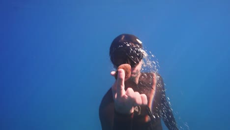 el hombre nada desde las profundidades del océano sosteniendo una roca, la luz brilla en la máscara