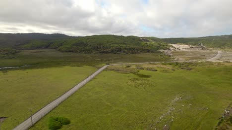 Aerial-orbit-of-a-land-route-in-a-lonely-meadow-in-Cucao-Chiloe-Chile,-cloudy-and-shady-day