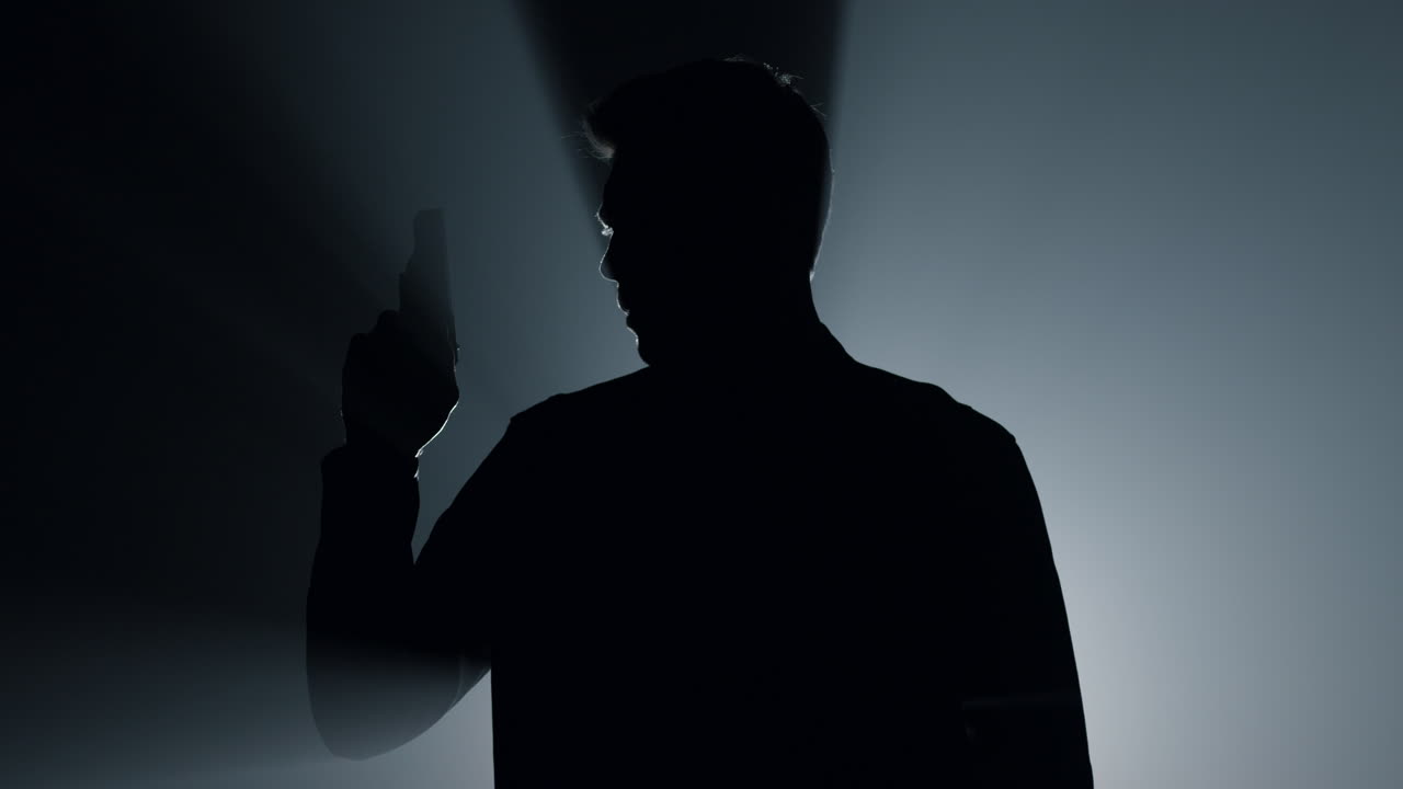 어 속에서 권총을 들고 손을 들고 있는 실루 총사. 범죄자가 총을 들고 있다.