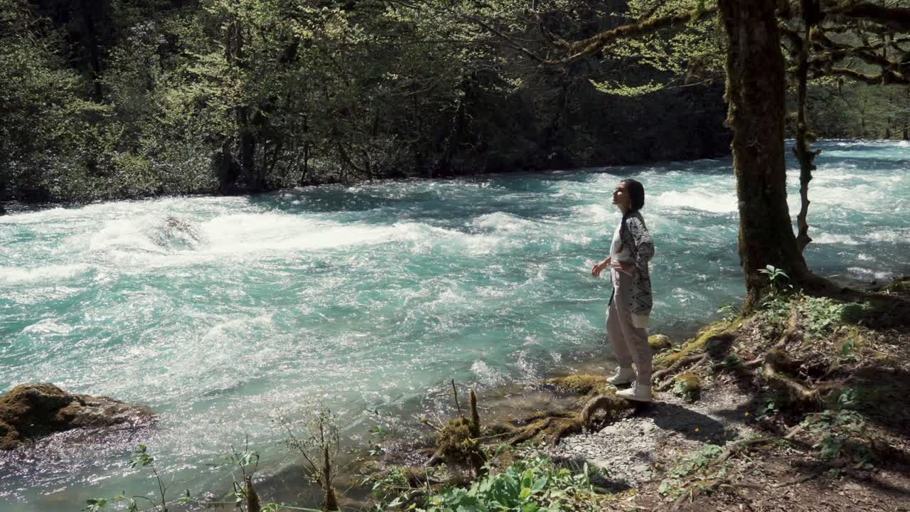 mujer de pie junto a un río en un bosque