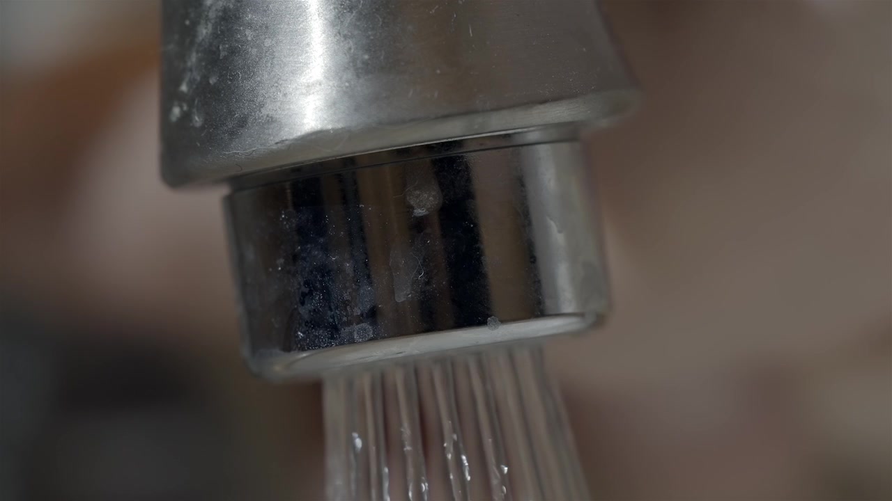 Primo piano estremo di un aeratore sporco del rubinetto del bagno con acqua corrente.
