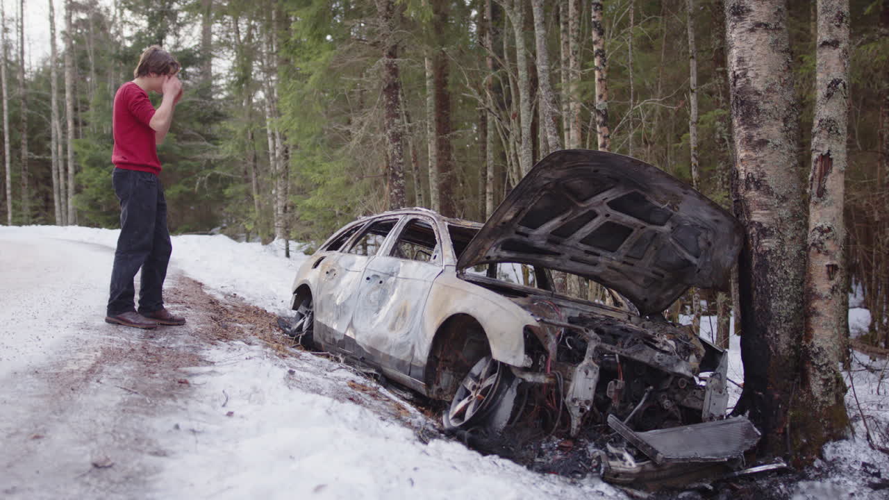 Emotional young man next to crashed and burnt car wreckage on icy roadside