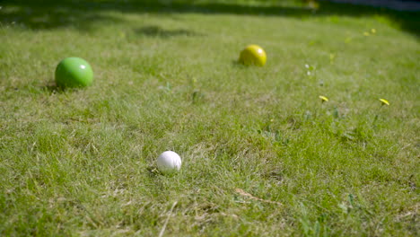 nahaufnahme von drei bunten pétanque-kugeln auf dem rasen, dann wirft der spieler einen weiteren ball in die nähe