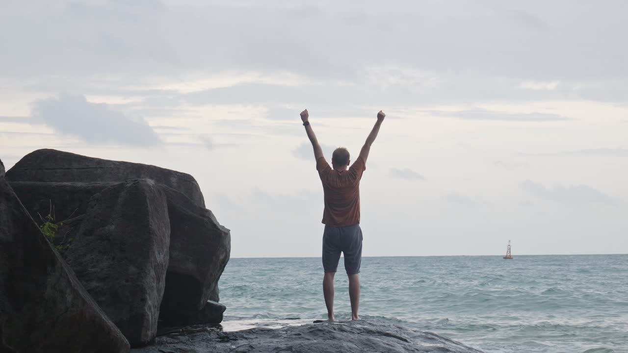 vista oscura de un turista masculino levantando los brazos en la playa rocosa de dam trau, isla de con dao, vietnam