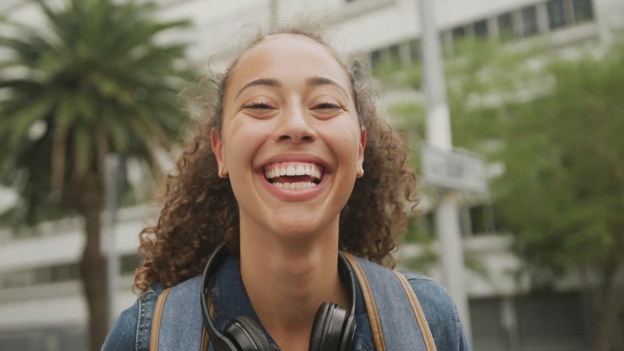 retrato de una feliz mujer biracial en la ciudad, con auriculares y sonriendo