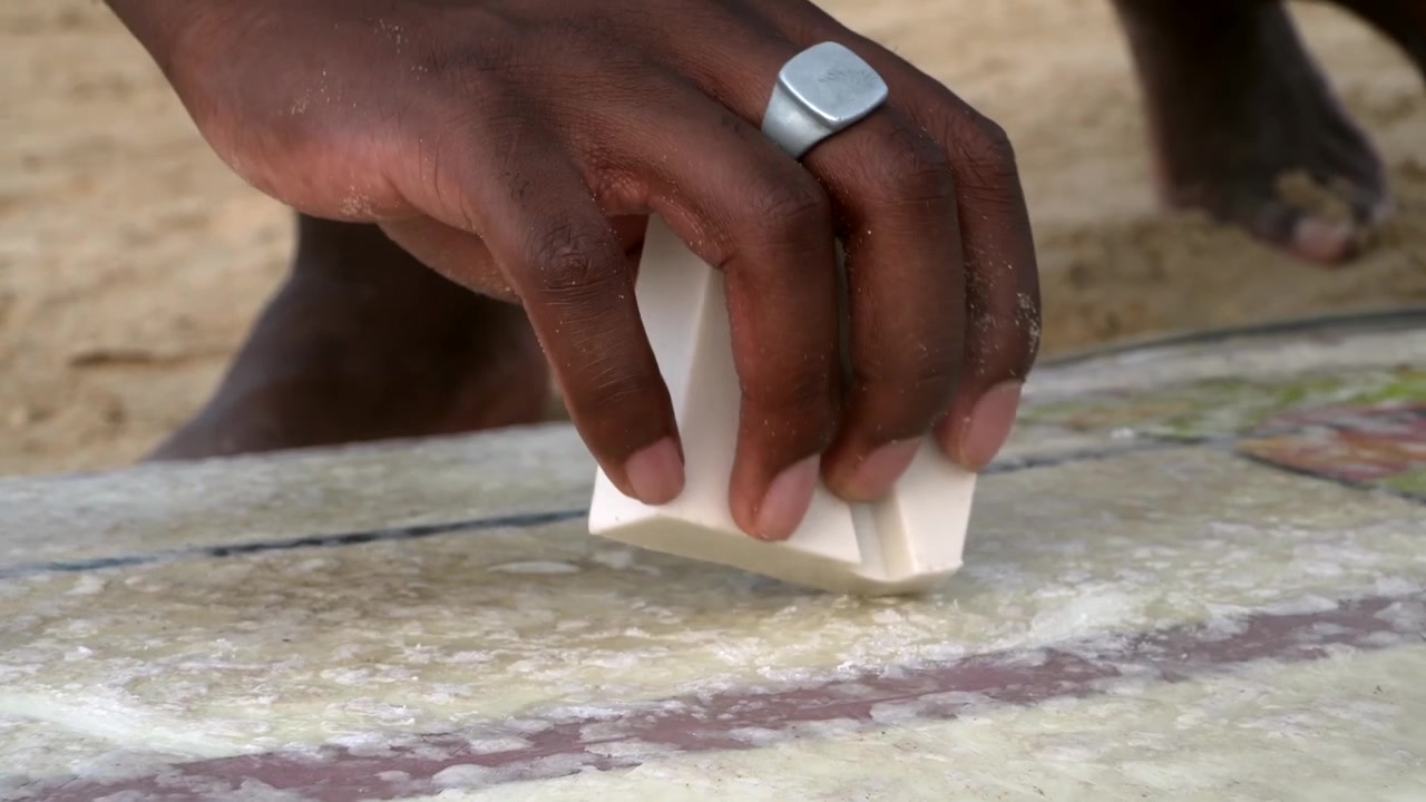 Surfer Applying Wax to Surfboard on the Beach