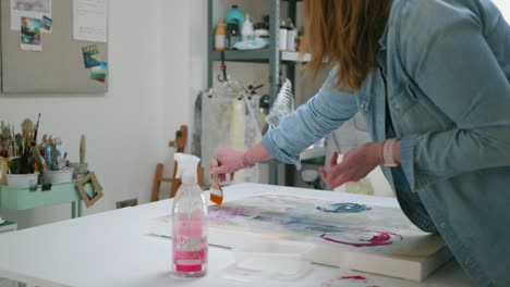 Female-artist-brushing-glue-on-paper-asset,-on-canvas,-in-a-home-studio