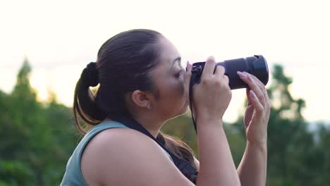 mujer con cámara dslr en sus manos, tomando fotos al aire libre durante el atardecer