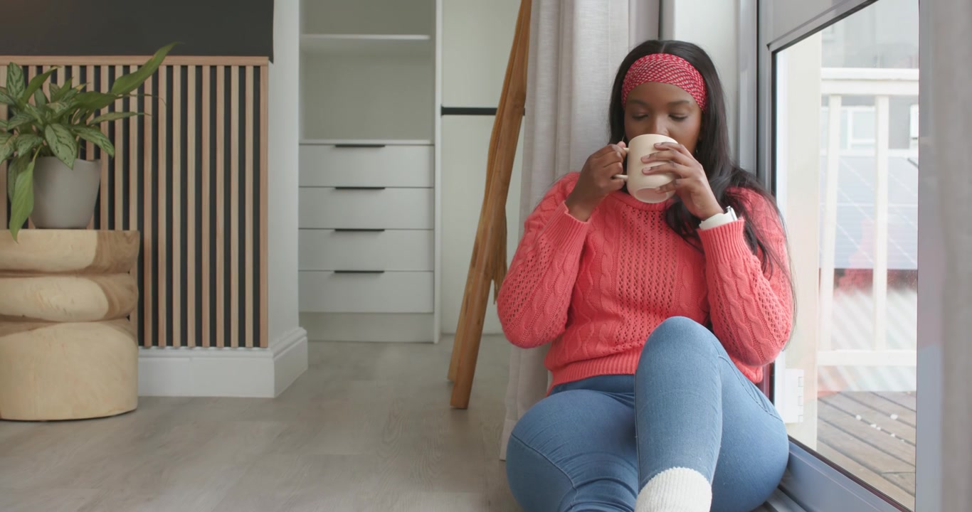 Donna afroamericana che aggiusta la presa e sorseggia una bevanda da una grande tazza al posto vicino al finestrino